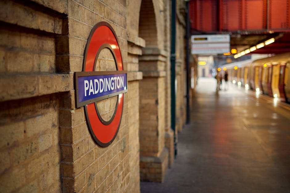 A daytime view of Farringdon station with train tracks running through the underground platform area. The platform has a smooth, grey concrete surface with tactile paving along the yellow safety line 